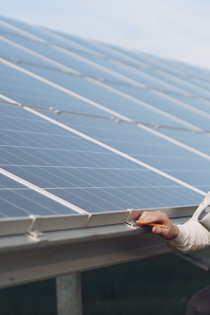 Focused young male employer in formal wear and hardhat working on solar panel station and checking details of modules